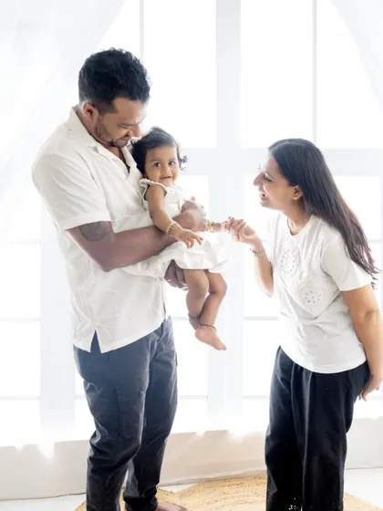 A candid family moment, with the mother playfully interacting with her daughter held by the father.