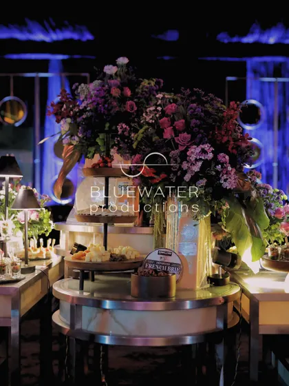 A beautifully styled food station, with a large floral arrangement cascading over a tiered display of cheeses and appetizers.