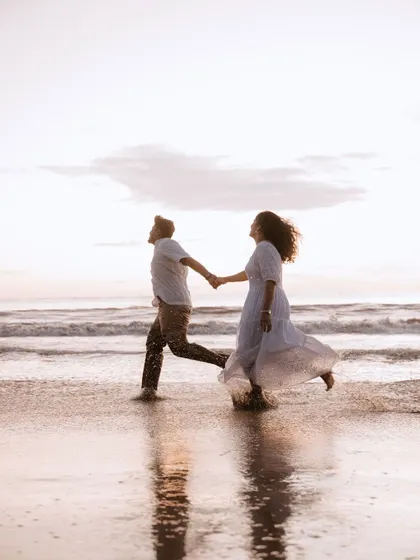 A beautiful silhouette of a couple running on the beach at sunset, their reflection captured in the wet sand.