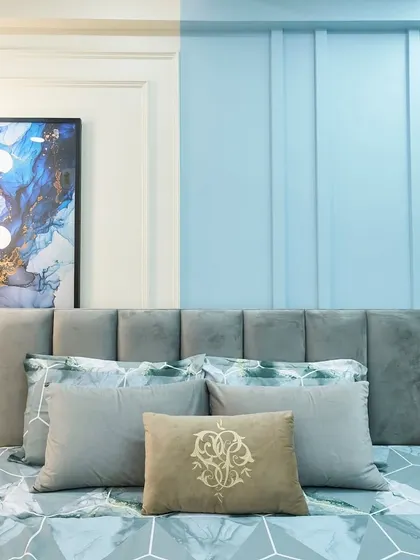 A close-up of the blue and grey themed bedroom. The abstract art and modern pendant light add a contemporary touch to the space.