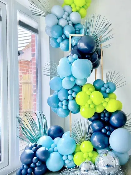 A creative collision of balloons, disco balls, and tropical leaves. This vibrant blue and lime green balloon installation is a party masterpiece, perfect for a modern and energetic celebration.
