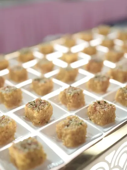 Bite-sized squares of a traditional Indian sweet, possibly a milk-based barfi, are presented on an illuminated tray. The grid-like arrangement creates a clean, contemporary look for the dessert counter.