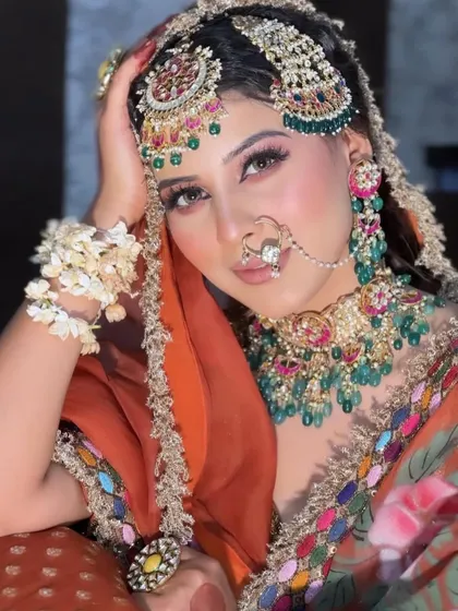 A regal and powerful bridal portrait. This look features heavy, traditional jewelry with green accents, paired with perfectly sculpted makeup and a confident gaze.