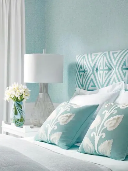 A delicate, light blue textured pattern on the wall complements the geometric headboard in this bedroom. This technique adds subtle visual interest without overwhelming the serene and calming atmosphere of the space.