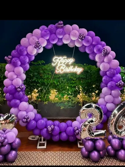 A vibrant purple-themed 26th birthday. This outdoor setup features a full-circle balloon arch, a neon sign, and silver number balloons.
