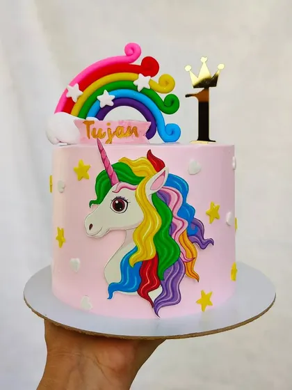 A magical unicorn and rainbow cake for a first birthday. The colorful unicorn and rainbow are made from fondant and placed on a pretty pink buttercream cake.