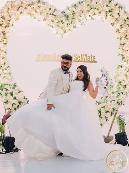 The couple strikes a pose at their beachside celebration, perfectly framed by the floral heart.