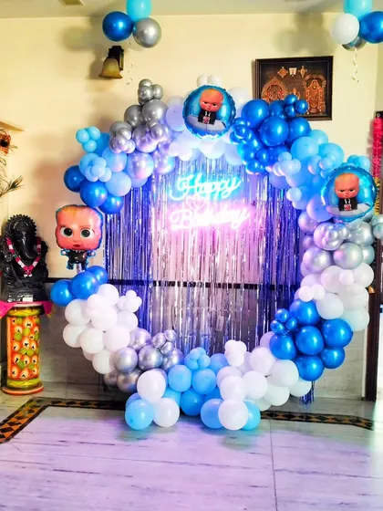 A Boss Baby themed birthday setup in a home. This decoration features a circular balloon arch in blue, white, and silver, with a shimmering tinsel curtain and a neon sign, perfect for a cool photo booth.