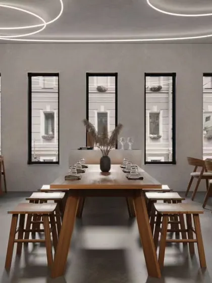 This minimalist dining space is designed for communal eating, centered around a large wooden table. The circular LED ceiling lights and stark, vertical windows create a contemporary and almost gallery-like atmosphere.