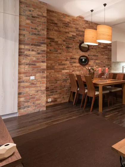 This design blends rustic and industrial elements, featuring an exposed brick wall, a simple wooden dining set, and modern pendant lights for a warm, loft-style feel.