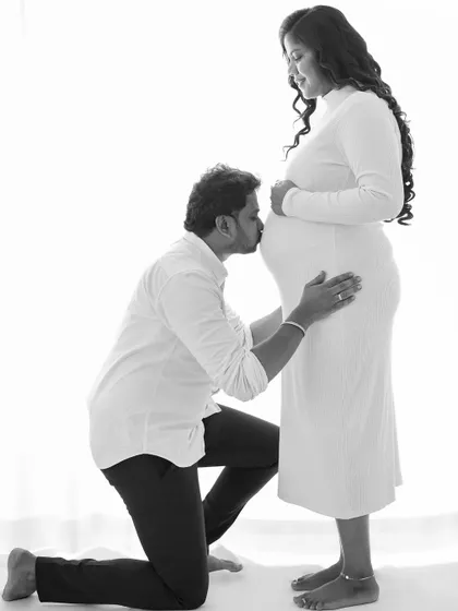 A classic pose in maternity photography, where the partner lovingly kisses the baby bump. This black and white shot emphasizes the emotion and anticipation of fatherhood.