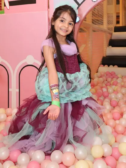 A birthday girl in a beautiful dress shows off her new temporary tattoo in the ball pit.