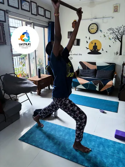 A client uses a staff to deepen her stretch in a warrior pose variation. Props like these help improve alignment, balance, and body awareness.