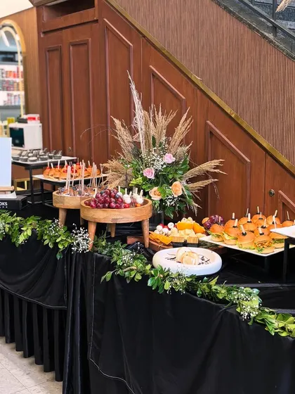 An elegant grazing table setup for a Looks Salon launch event. The display is styled with a dramatic black velvet cloth and lush greenery, featuring tiered platters of caprese skewers, mini burgers, and a curated cheese board.