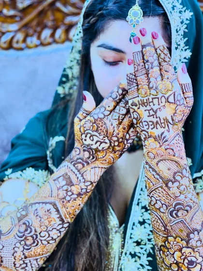 The bride's hands framing her face, a beautiful way to showcase both her henna and her delicate features.