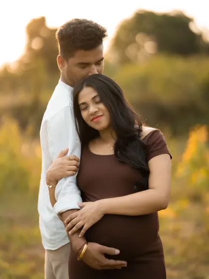 An intimate moment between an expecting couple, captured outdoors during golden hour. The warm light creates a romantic and gentle mood.