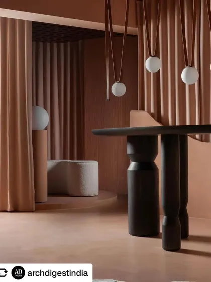 The strategic use of drapes allows the space to be flexible, creating partitions or revealing new areas. Here, they frame a view of hanging spherical lights and a custom-designed table.