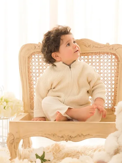 Looking up with wonder. Seated in a classic rattan chair, this little boy's curious upward gaze adds a touch of innocence and charm to his first birthday portrait.