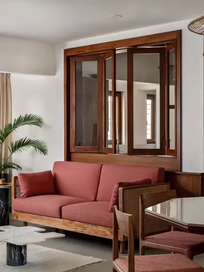 The cozy family lounge, featuring a sofa in 'Indian red' fabric that adds a subtle desi touch to the Japandi style. A bifold window behind the sofa creates an effortless connection to the kitchen.