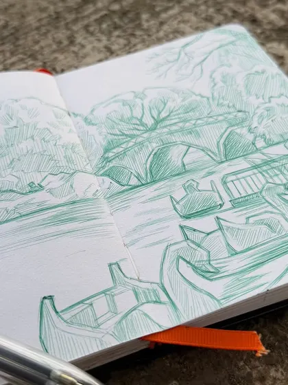 A close-up view of my sketchbook and the 4-in-1 ballpoint pen I used for this landscape drawing. You can see the cross-hatching and line work that create texture and depth in the trees and water.