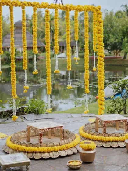 A beautiful Haldi setup by the water, with low seating and hanging marigold garlands.