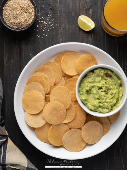 Healthy quinoa chips paired with fresh guacamole. The dark wooden background makes the bright green of the dip stand out, and the overall styling feels both wholesome and delicious.