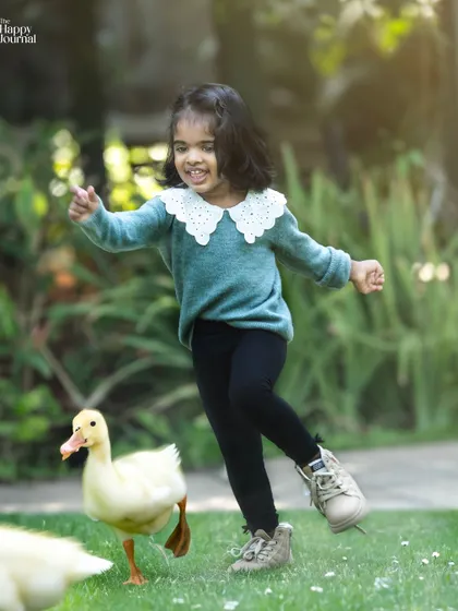 A little girl's joyful playtime with a duckling. This outdoor photo is a wonderful example of capturing authentic, happy moments with animals.
