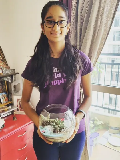 A young girl with her completed terrarium, featuring carefully layered sand and succulents. These workshops are a great way to introduce children to the world of plants.