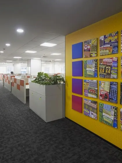 A bright yellow accent wall at the Scientific Games office features a curated gallery of the company's products. This serves as both a vibrant design element and a constant reminder of the team's creative output and success.
