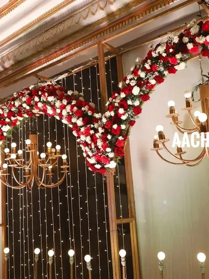 A closer view of the floral arches, made with red and white roses. The combination of the flowers, the warm light from the chandeliers, and the fairy light curtain creates a rich and festive look.