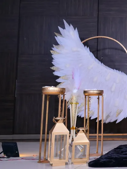 A close-up of the props used at the baptism, including gold-toned lanterns and stands, which complement the main angel wing decor.