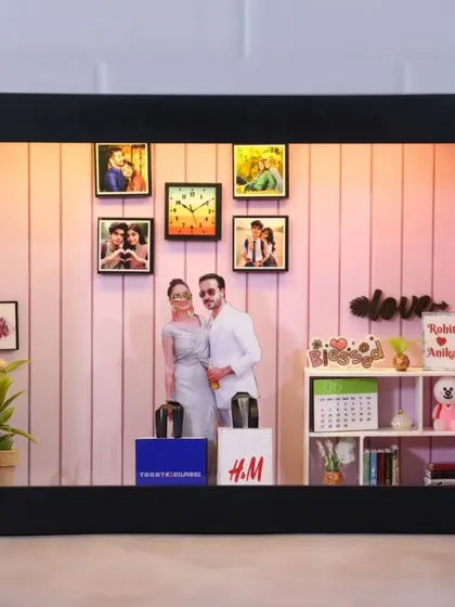 A couple's miniature theme box with shopping bags from H&M and Tommy Hilfiger, a calendar, and a 'love' sign, all set in a beautifully lit miniature room.