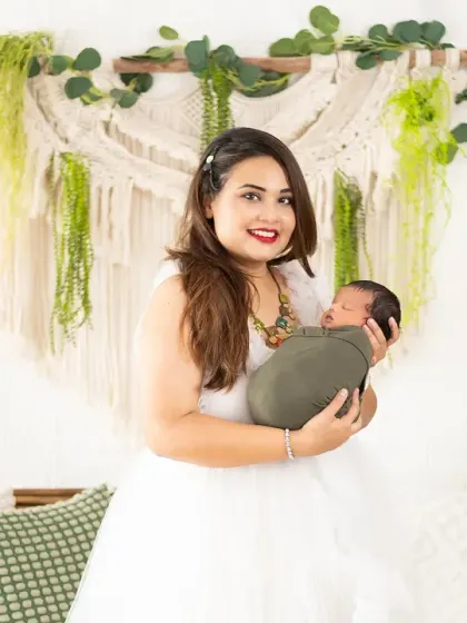 A proud new mother holds her sleeping baby. This portrait, taken in our greenery-filled boho set, feels fresh, natural, and full of life.