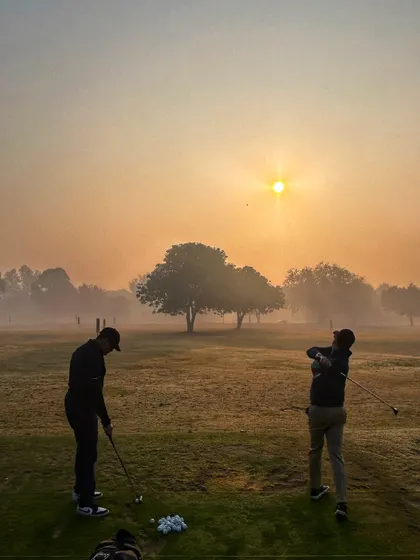Two golfers practice on the grass tees as the sun rises through the morning mist.