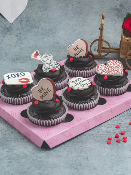 A box of our special Valentine's Day chocolate cupcakes. Each one is topped with a cute, edible message like "Be Mine" and "XOXO".