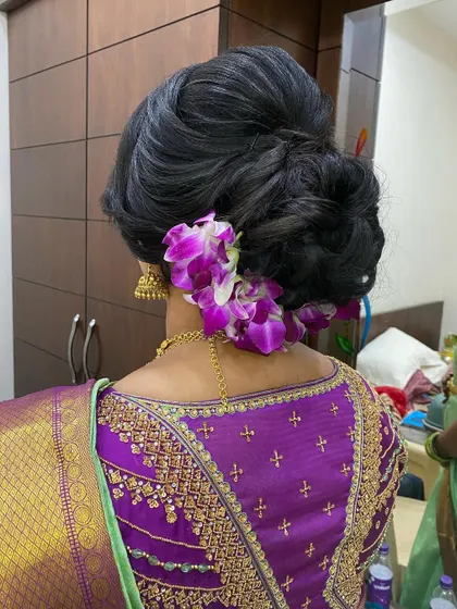 A voluminous, textured updo decorated with beautiful purple orchids. Using unconventional flowers like orchids can add a unique and modern touch to a festive hairstyle.