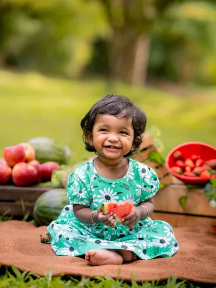 A fruit-themed picnic in the park. The vibrant colors of the fruit and the child's dress look beautiful against the lush green background.