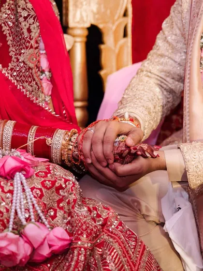 A close-up of the couple's hands during the wedding rituals, a symbol of their union. The bride's red choora and the groom's hand holding hers tell a story of love and commitment.
