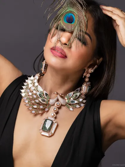 A creative beauty shot with a peacock necklace, with the model's eyes closed.