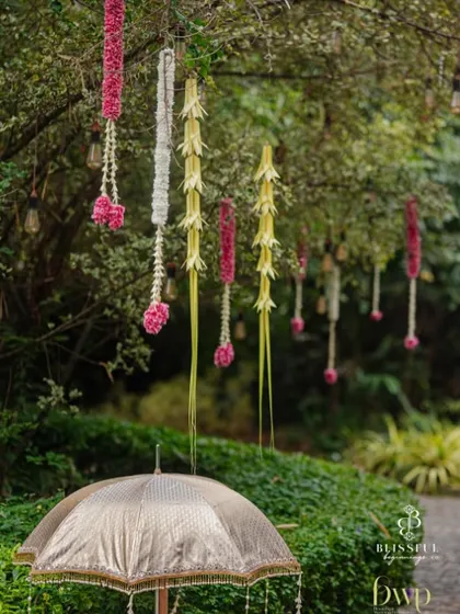 A closer view of the floral hangings on the tree. The combination of jasmine, pink flowers, and woven coconut leaves is a classic element of South Indian decor, beautifully integrated into the natural setting.