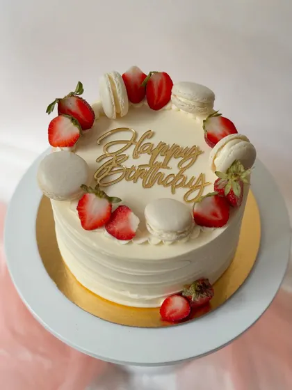 A simple yet elegant birthday cake. The smooth white buttercream is the perfect canvas for a crown of fresh strawberries and white macarons.