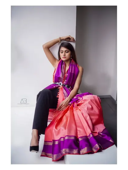 A full-body shot showcasing a unique saree drape. The pose is one of relaxed elegance, highlighting the fusion of traditional and contemporary styling.