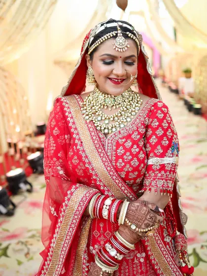 A beautiful, happy moment captured. The bride's smile shows her confidence, with her makeup looking fresh and radiant. The bold red lip and defined eyes are key elements of this traditional Indian bridal look.