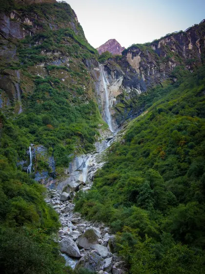 A wide view of a valley on the Annapurna trek, showing the scale of the landscape with its lush greenery and powerful waterfalls carving through the mountains.