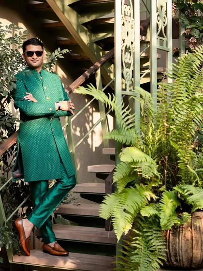 The groom looking sharp in his custom-designed bottle green sherwani. The self-embroidered fabric and gold buttons add a regal touch, while the setting among the ferns feels perfectly Goan.