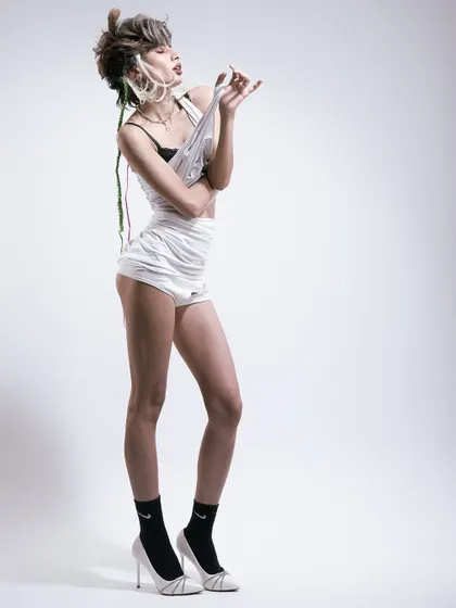 A deconstructed fashion look. The lighting is a simple, hard source from the side, creating a high-contrast image that highlights the texture and chaos of the styling.