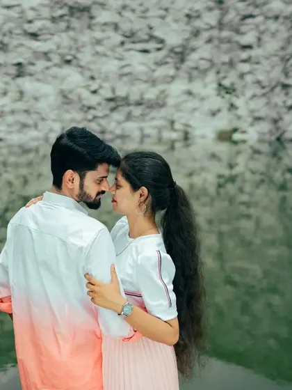 A close-up of a couple sharing an intimate moment by the water, with the textured rock wall as a backdrop. The focus is on their connection.
