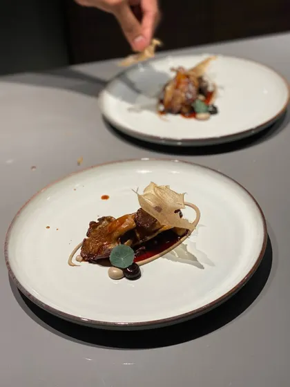 The final touch being added to a complex appetizer. This dish combines earthy mushrooms with a rich sauce and a delicate, crispy tuile.