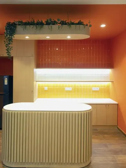 A modern pantry space featuring a fluted island counter and warm, recessed lighting against orange and yellow tiled backsplashes. This compact yet stylish area provides all necessary amenities for a quick coffee break.