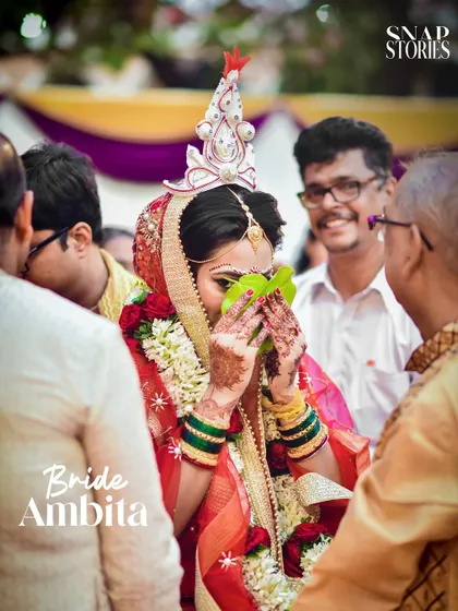 A Bengali bride participates in the Shubho Drishti ritual, hiding her face behind betel leaves. We have experience with diverse Indian wedding traditions and capture them authentically.